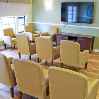 A cozy seating area with multiple chairs facing a large television in a well-lit room.
