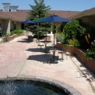 A sunny courtyard with outdoor seating, featuring tables and umbrellas near a small fountain.