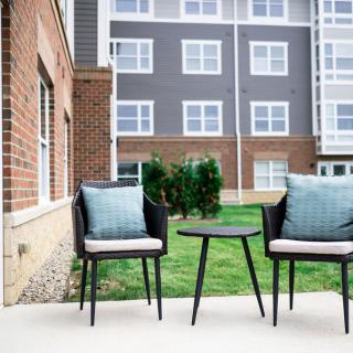 A cozy outdoor patio with two chairs and a side table in front of a modern apartment building.