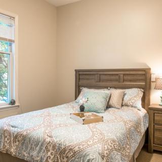 A cozy bedroom featuring a comfortable bed with decorative pillows, a lamp on the nightstand, and a window letting in natural light.