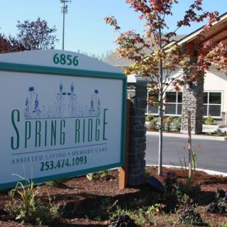 A sign for Spring Ridge in front of a building with landscaping.