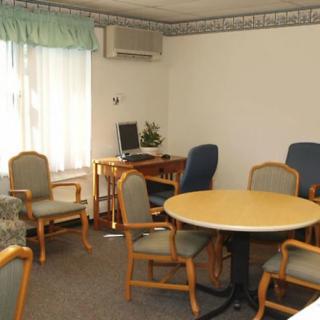 A small meeting room with a round table, several chairs, a window, and a computer on a desk.