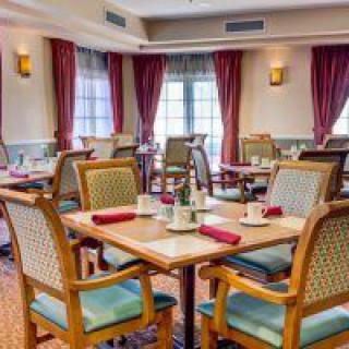 An elegantly furnished dining area with neatly arranged tables and chairs, complemented by rich curtains and warm lighting.