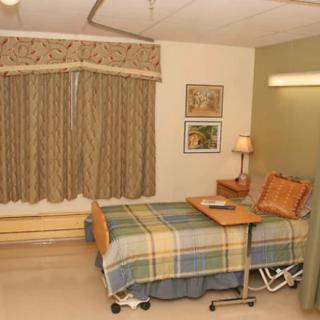 A hospital room with a single bed, curtains, and a bedside table with a lamp.