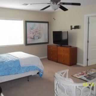 A cozy bedroom featuring a bed with blue bedding, a TV on a wooden cabinet, and a painting on the wall.