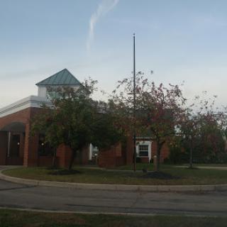 A view of a brick building with a flagpole and surrounding trees under a cloudy sky.