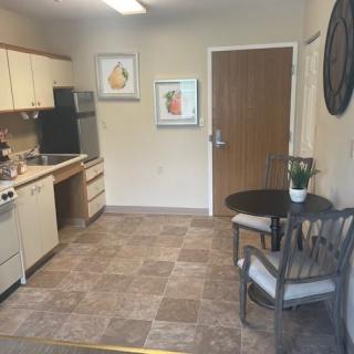 A cozy kitchen area with a small dining table and two chairs, featuring artwork on the walls and basic kitchen appliances.