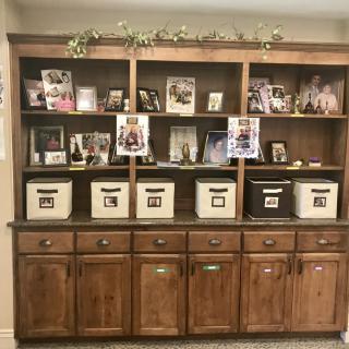 A wooden bookshelf displaying family photos and storage bins in a cozy home setting.