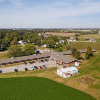 An aerial view of a rural landscape featuring farmland, a parking lot, and several buildings surrounded by greenery.