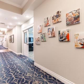 A well-lit hallway with patterned carpet and artwork displayed on the walls.