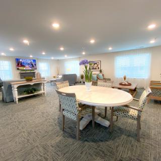 A cozy living room with modern furniture, featuring a round table and chairs, and a television mounted on the wall.