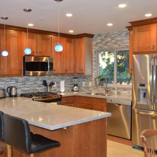 A modern kitchen featuring wooden cabinets, stainless steel appliances, and a central island with pendant lighting.