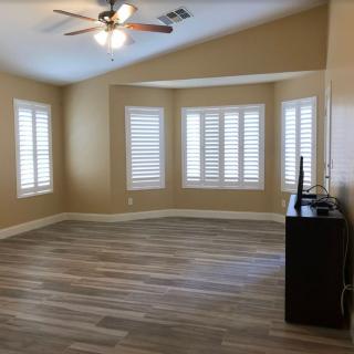 A spacious, empty room with hardwood flooring and large windows with shutters.