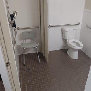 A view of an accessible bathroom featuring a toilet and a shower chair.