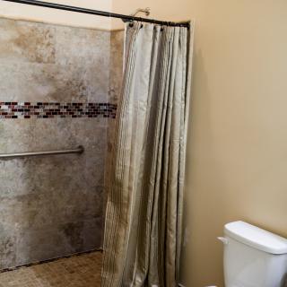 A bathroom featuring a tiled shower with a curtain and a toilet.