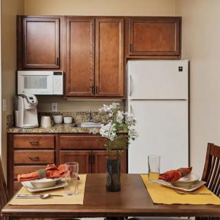 A cozy kitchen with wooden cabinets and a dining table set for two, featuring a white refrigerator and microwave.