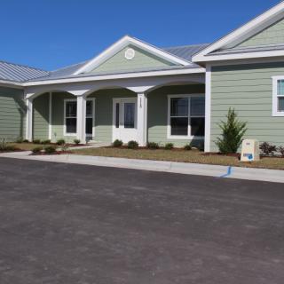 A single-story green residential building with a clean, paved driveway and neatly landscaped surroundings.