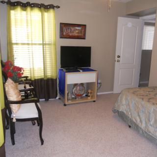 A cozy bedroom with a television, chair, and bright curtains.