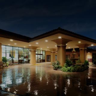 A beautifully lit hotel entrance on a rainy night, showcasing modern architecture and serene landscaping.