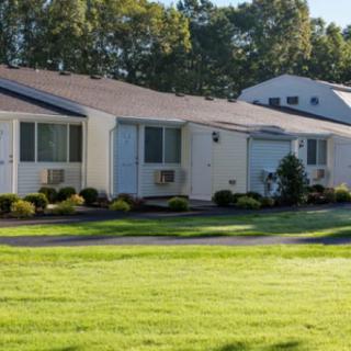 A row of suburban homes with well-maintained lawns and trees in the background.