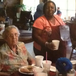 An elderly woman and a caregiver enjoying a meal at a dining area.