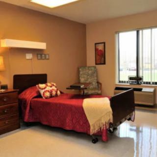 A cozy single-bed room with a window, chair, and bedside lamp.