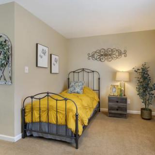 A cozy bedroom with a metal bed frame and bright yellow bedding, complemented by tasteful decor and greenery.