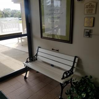An indoor bench beside a window and door, with a framed picture and plaques on the wall.