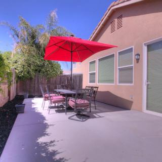 A sunny backyard patio with a table, chairs, and a red umbrella.