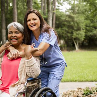 A nurse and an elderly woman in a wheelchair enjoy time outdoors together.