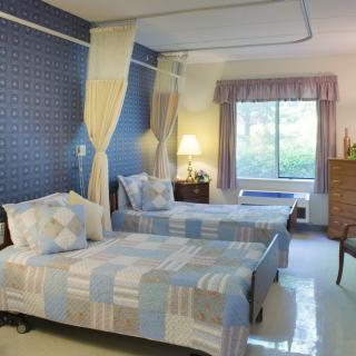 A cozy hospital room with two twin beds, decorated in soft colors and featuring a large window.