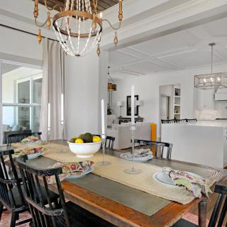 A modern dining area with a view into the kitchen, featuring elegant table settings and a chandelier.