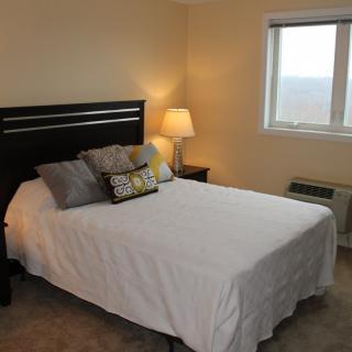 A cozy bedroom with a neatly made bed, a bedside lamp, and a window.