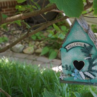 A decorative birdhouse with a welcome sign hanging in a lush garden.