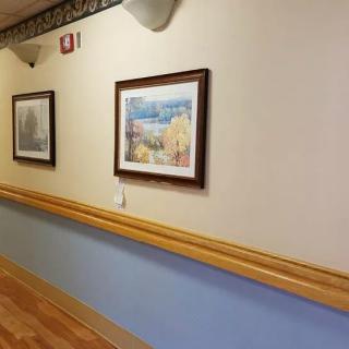 A hallway with framed paintings and a wooden handrail on the wall.