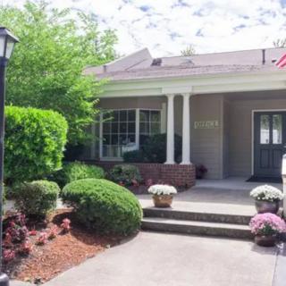 A well-maintained house with a front porch, surrounded by neatly landscaped gardens and trees.