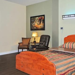 A hotel room featuring a bed, comfortable chairs, a lamp, and wall art.