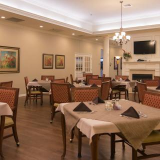 An elegant dining area with neatly arranged tables and chairs, a chandelier, and a fireplace.