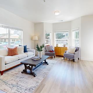 A bright and modern living room with a sofa, chairs, and a coffee table, accented by large windows allowing natural light.