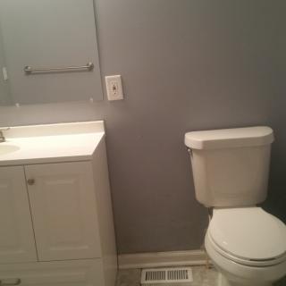 A simple bathroom with a toilet, sink, and cabinet against gray walls.