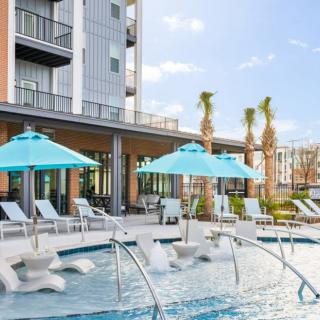 A modern outdoor pool area at a hotel, featuring lounge chairs and umbrellas amidst palm trees.