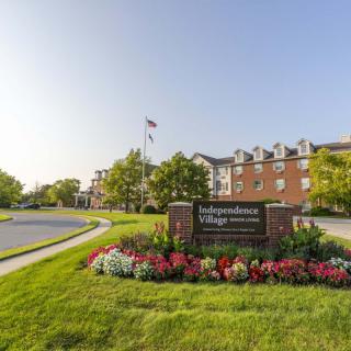 A well-maintained community entrance with a sign reading 'Independence Village' surrounded by flowers and greenery.