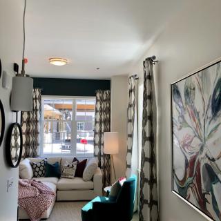 A cozy living room with stylish decor, featuring a comfortable sofa, large window with patterned curtains, modern wall art, and ambient lighting.
