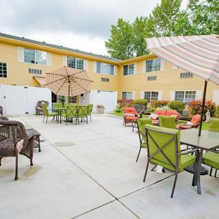 A spacious outdoor patio area with seating and umbrellas, surrounded by a building and greenery.
