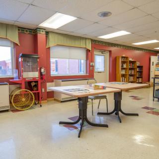 An empty classroom with tables, chairs, bookshelves, and a popcorn machine.