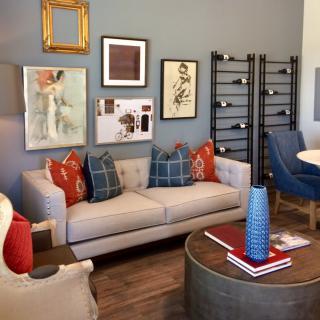 A stylish living room with a gray sofa, decorated with colorful pillows and surrounded by various artworks and a modern coffee table.