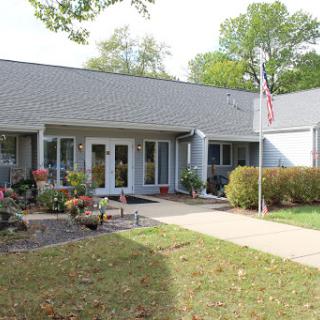 A welcoming entrance to a facility, featuring well-maintained landscaping and an American flag.