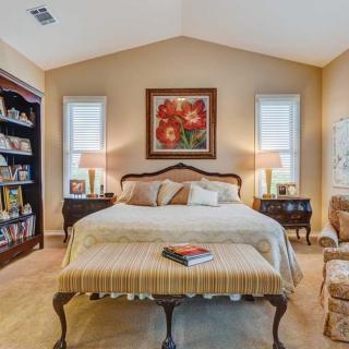 A cozy bedroom with elegant furniture, artwork above the bed, and a well-stocked bookshelf.