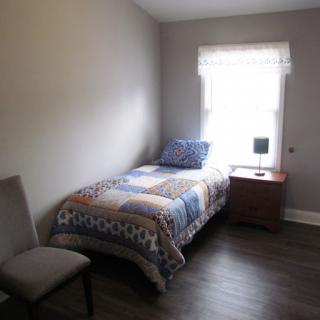 A cozy, minimalist bedroom featuring a single bed with patterned bedding and a wooden nightstand.