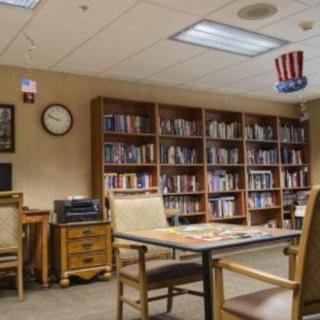 A cozy library space with bookshelves, tables, and chairs for reading.